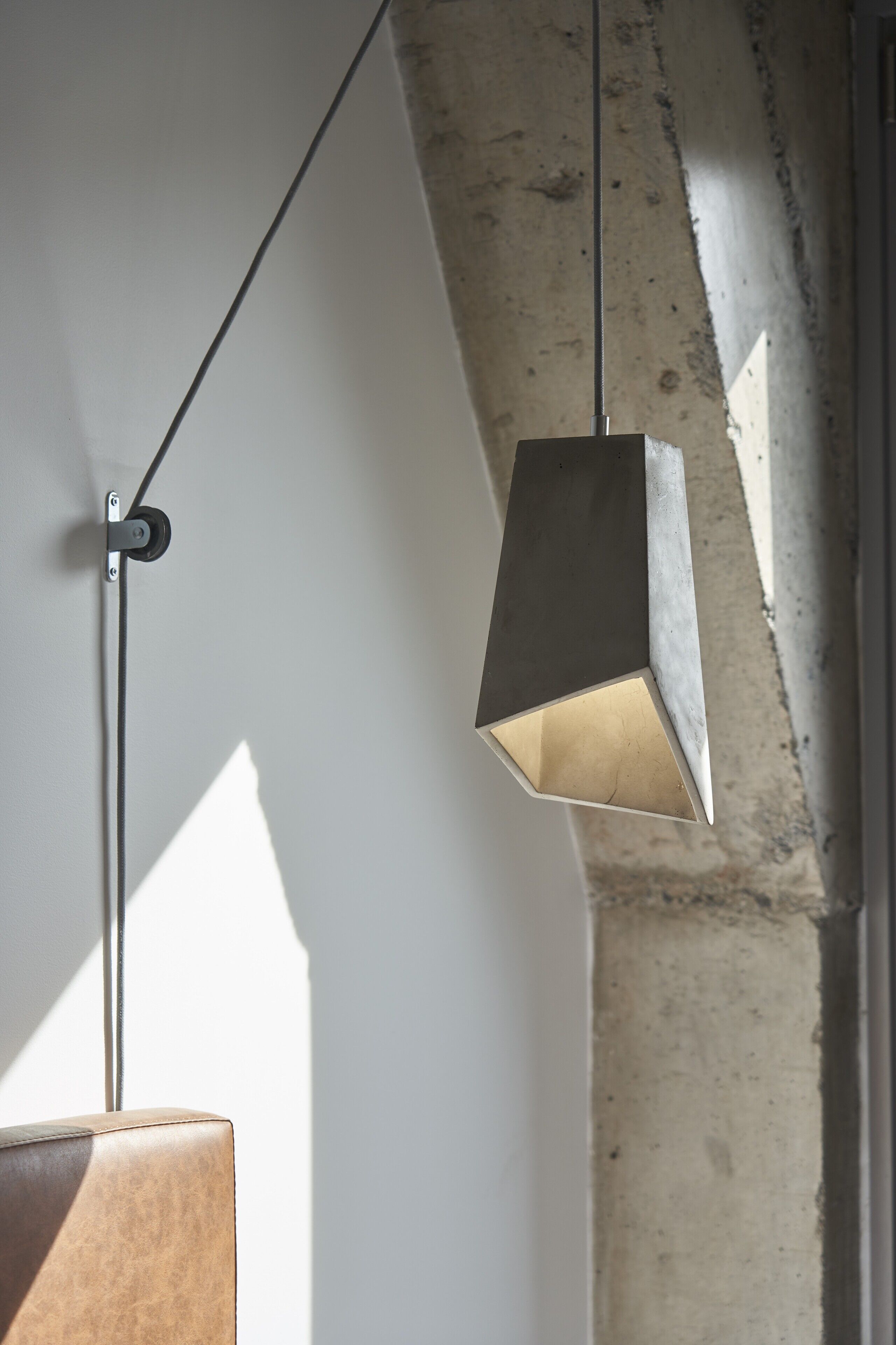 A pendant light fixture with a geometric design, mounted on a wall with a concrete texture.
