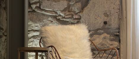 A chair with a fluffy white cushion against a stone wall.