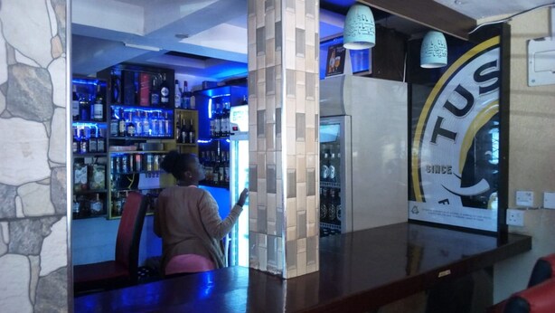 Eine Bar mit Regalen voller Flaschen, einer Theke mit einem Schild und einer Steinwand.