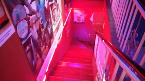 Eine Treppe mit roter Beleuchtung, eine Wand mit Plakaten und ein Geländer.