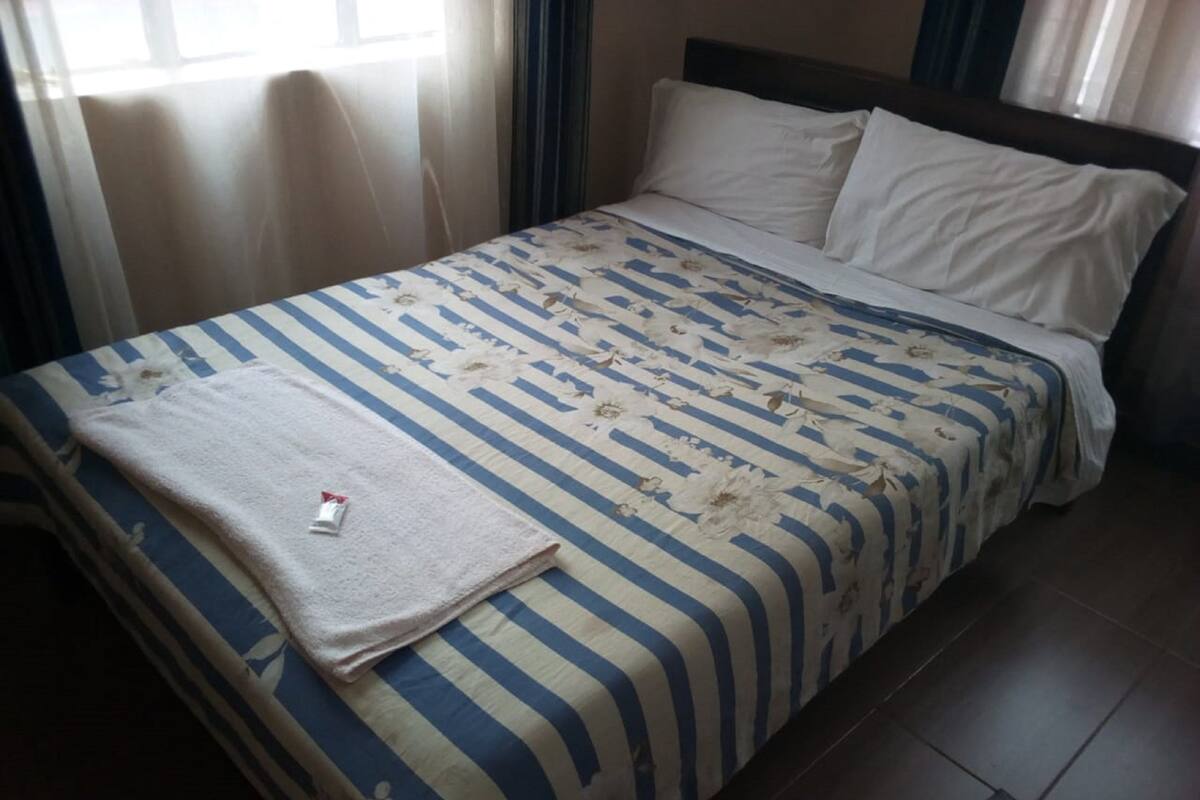 Una cama con una colcha a rayas y almohadas, una toalla blanca y un objeto pequeño sobre la cama.