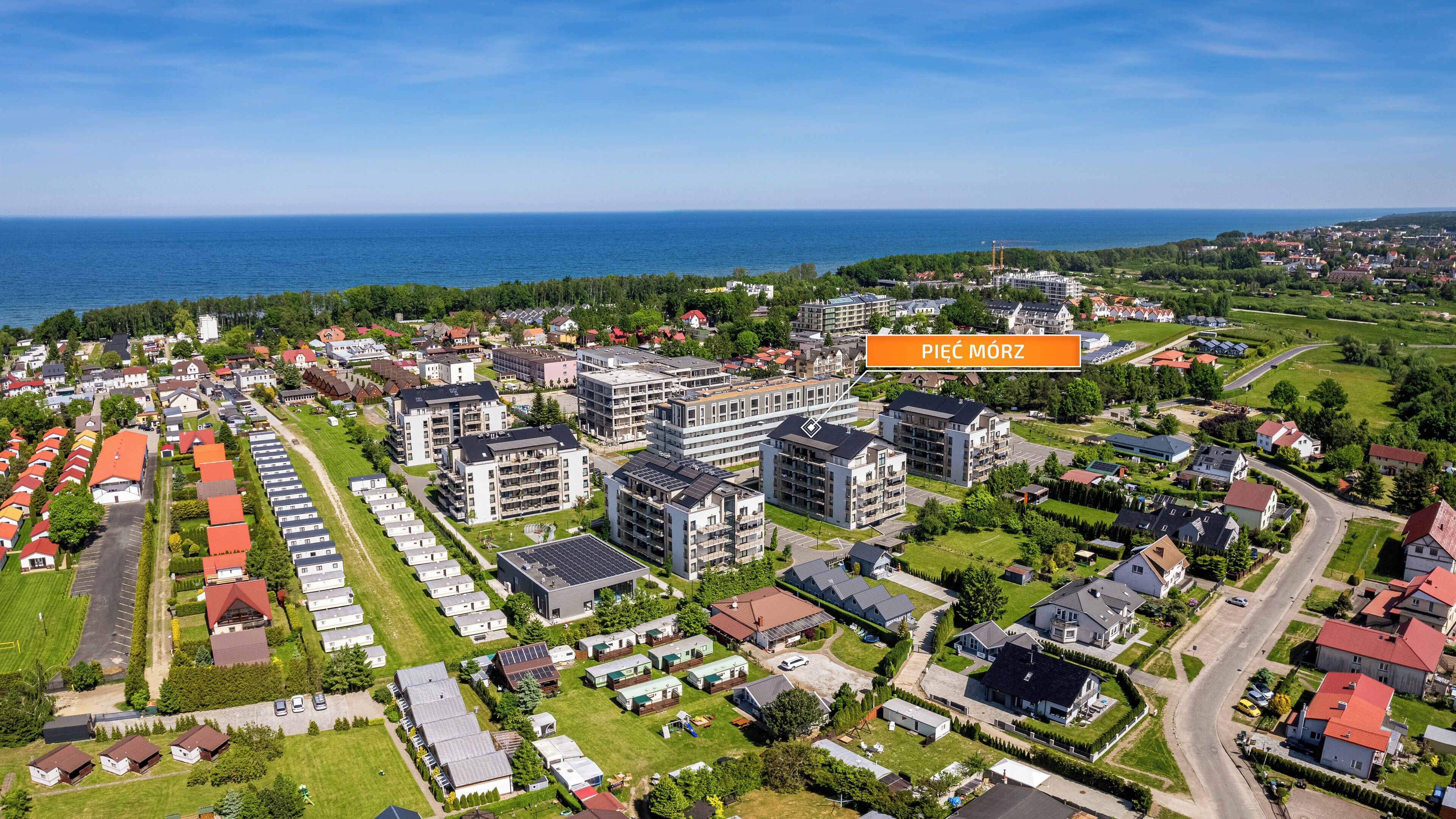 An aerial view of a residential area with modern apartment buildings, a marina, and a clear view of the sea.