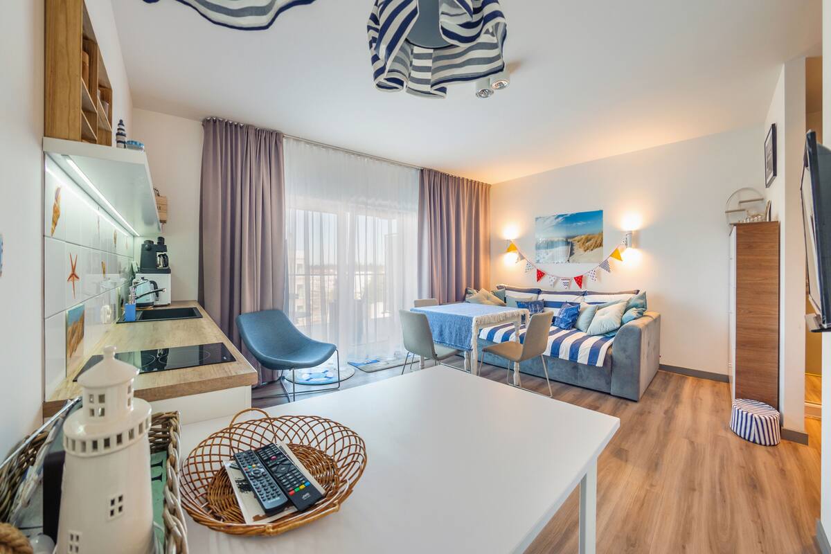 A modern hotel room with a dining area, a sofa set, a coffee table, and a kitchen area with a kettle.