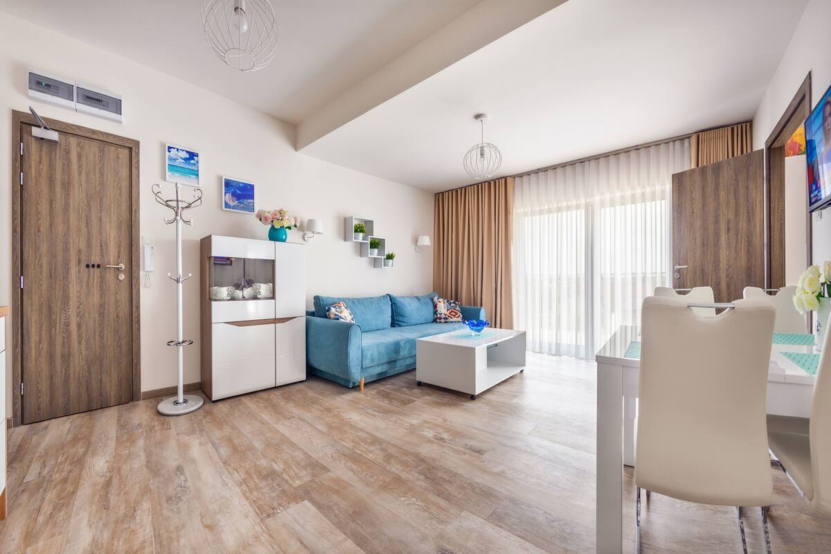 A modern living room with a blue sofa, white coffee table, and a dining area with a white chair.