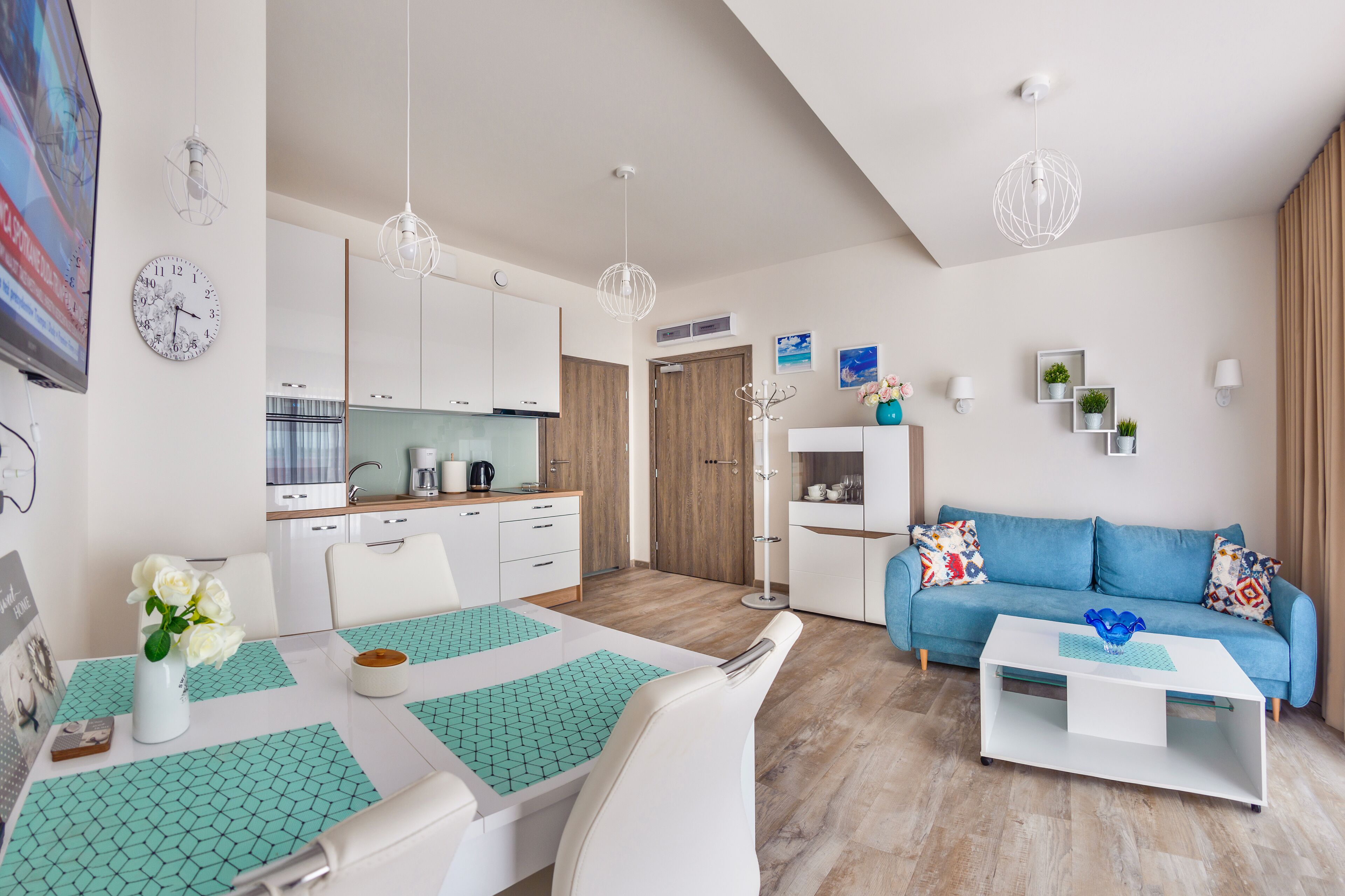 A modern living room with a blue sofa, white coffee table, and a dining area with a white table and chairs.