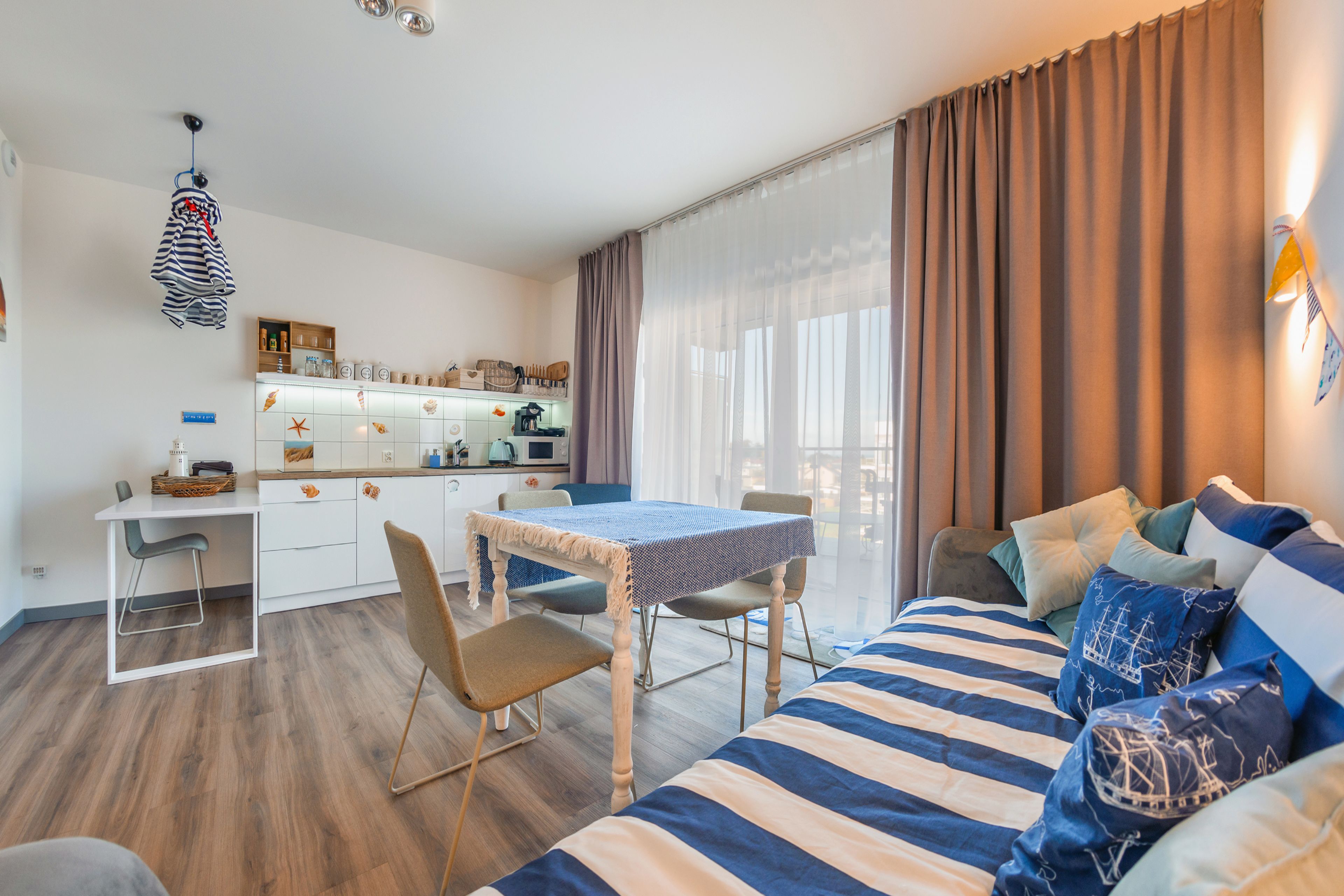 Una habitación moderna y luminosa con comedor, una cama con ropa de cama a rayas y un ventanal con cortinas.