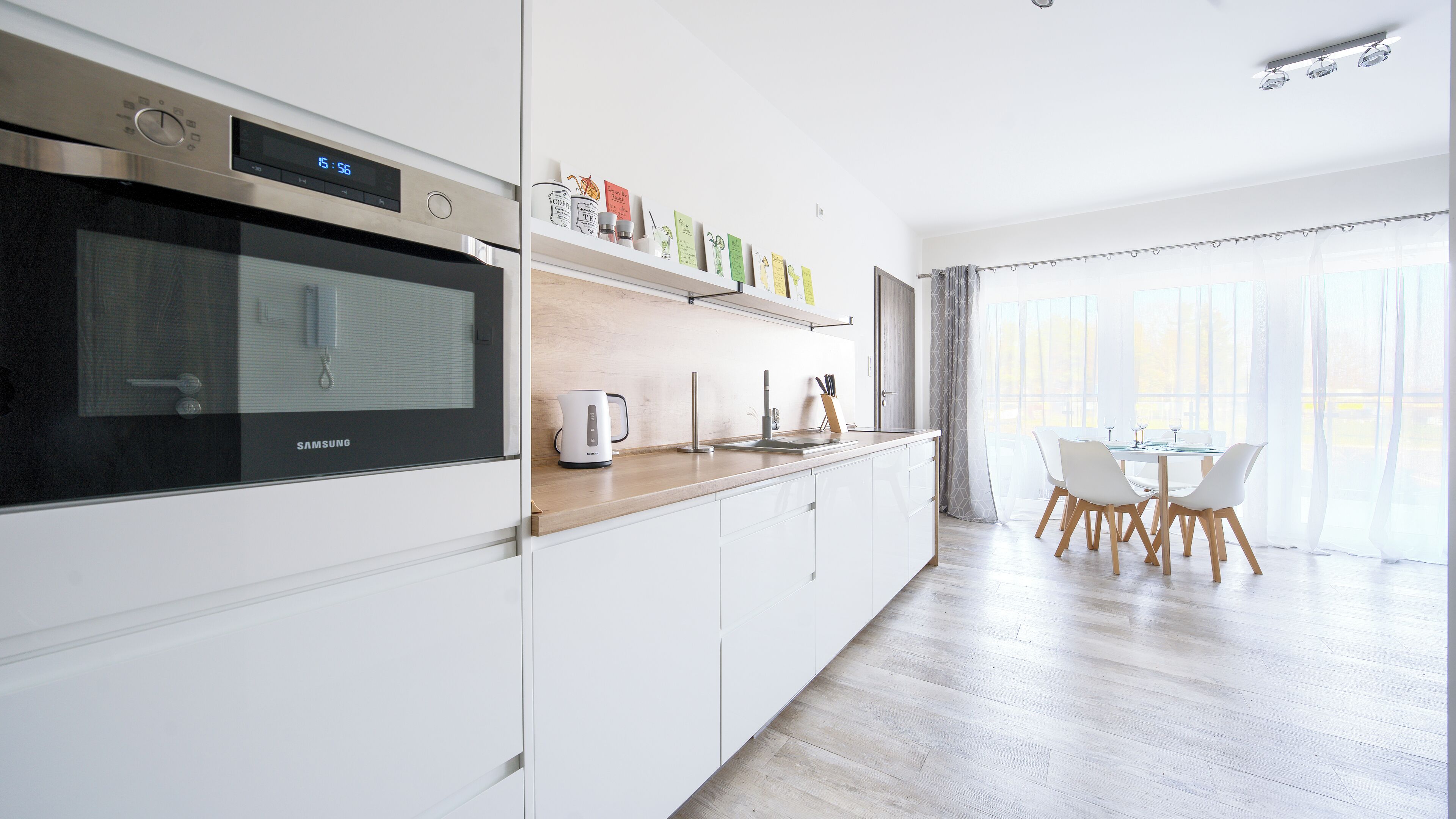 A modern kitchen with a built-in oven, a coffee maker, and a dining area with a table and chairs.
