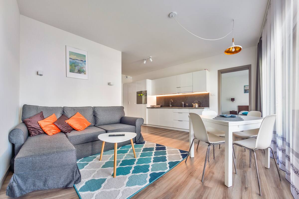 A modern living room with a grey sofa, a small white table, and a patterned rug.