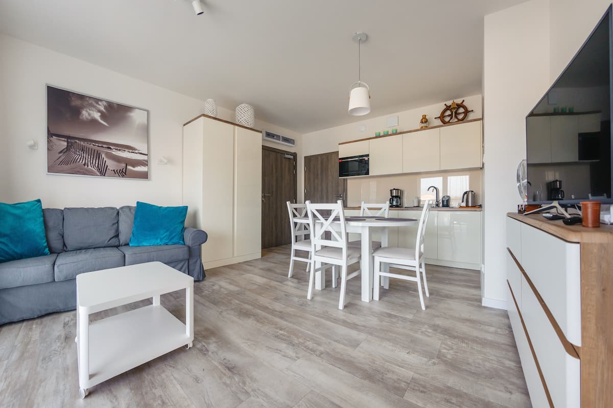 A modern living room with a grey sofa, white coffee table, and a dining area with a white table and chairs.