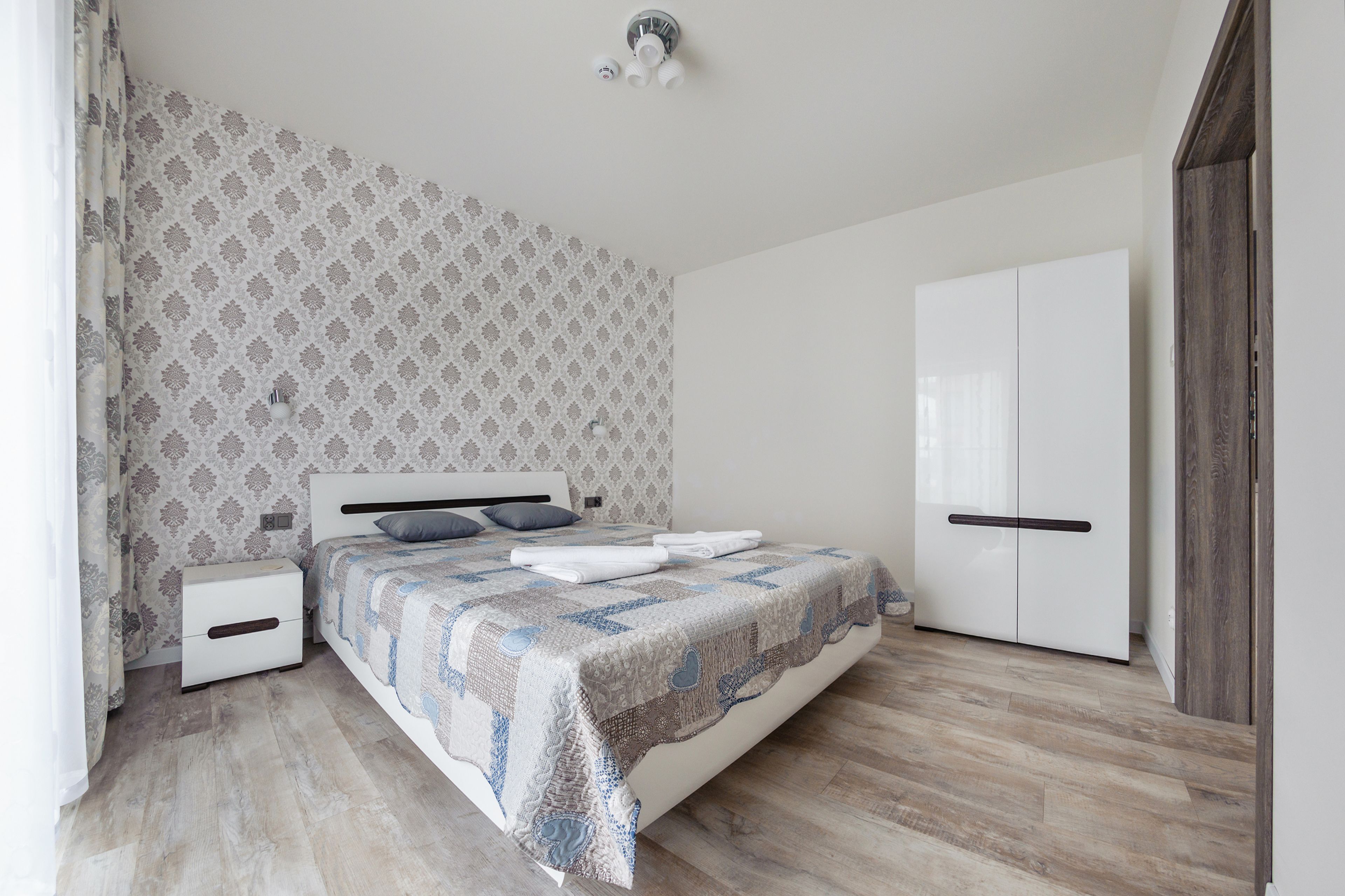 A bedroom with a bed, nightstands, a wardrobe, and patterned wallpaper.