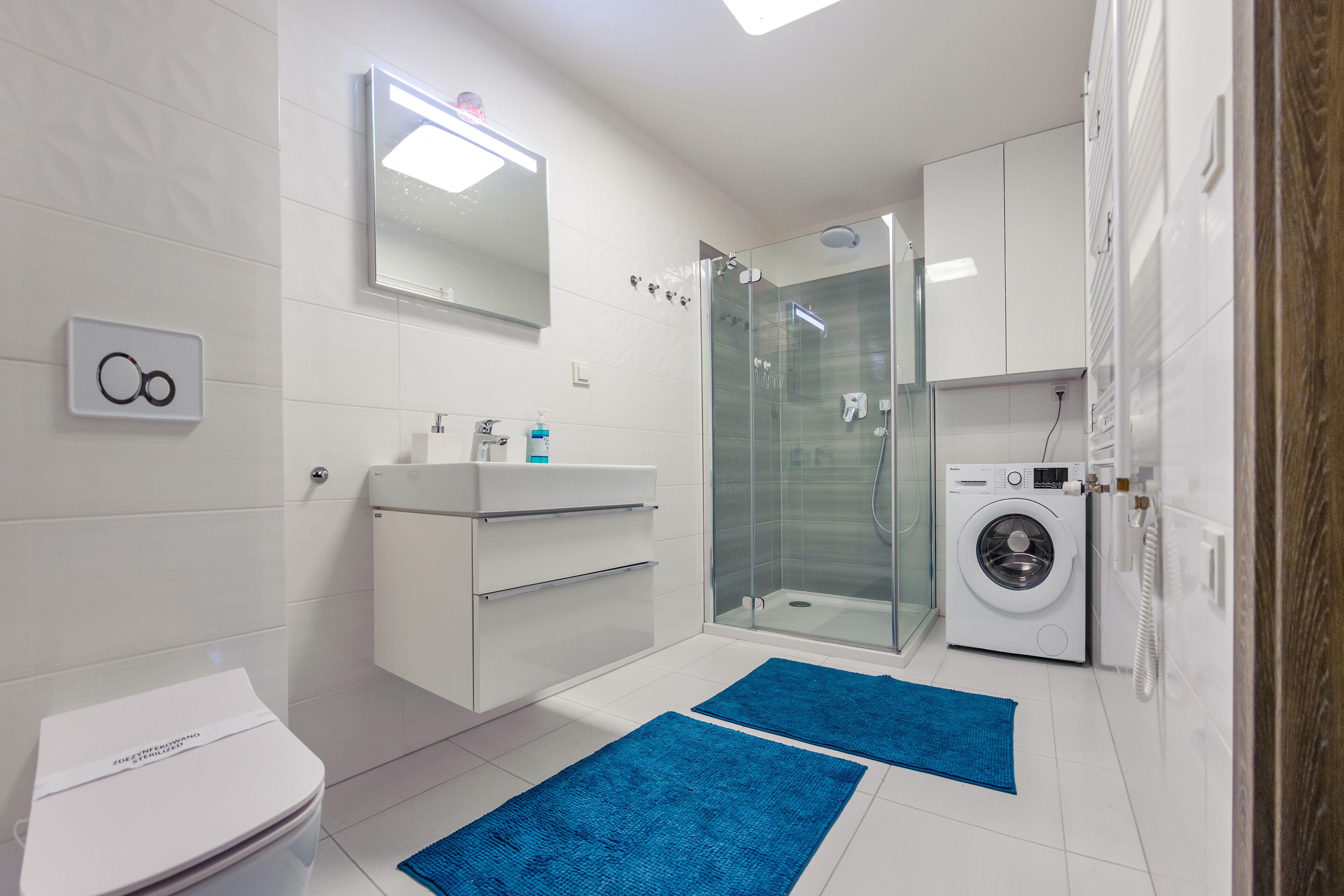 A modern bathroom with a toilet, sink, mirror, shower, and washing machine.