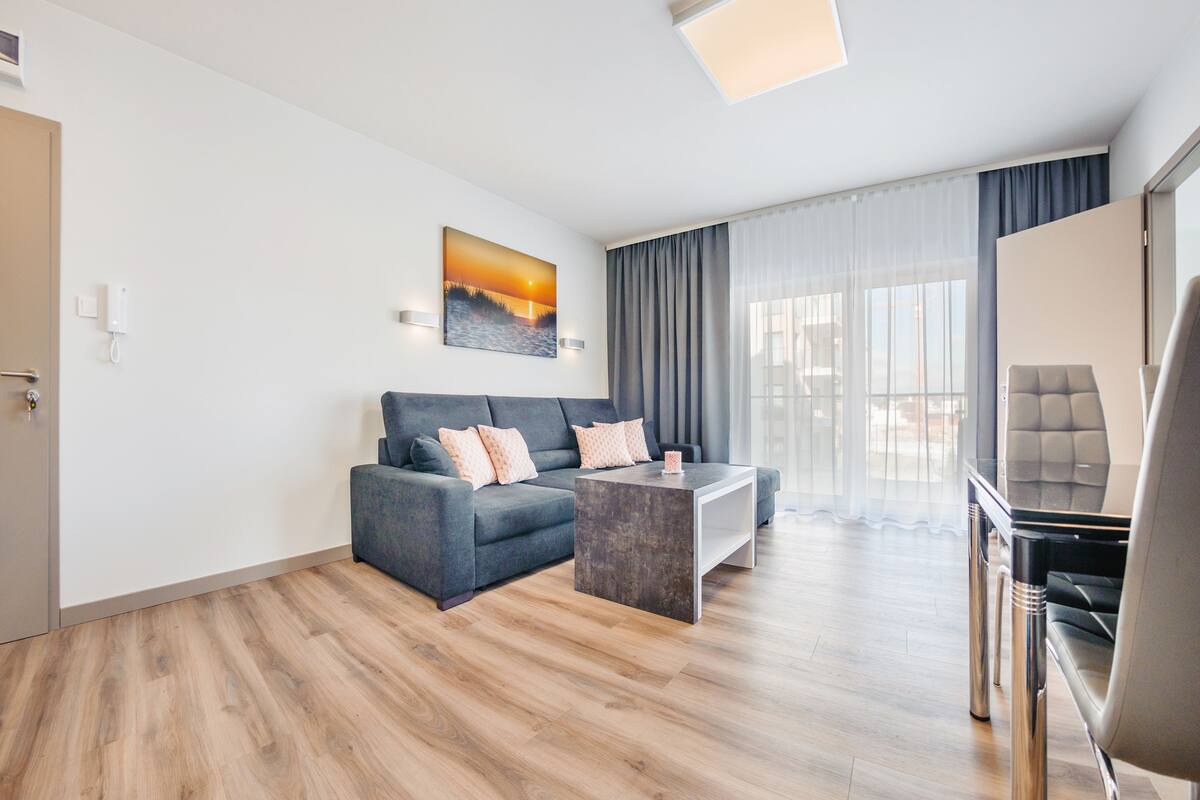 A modern living room with a grey sofa, a coffee table, and a dining area with a chair.