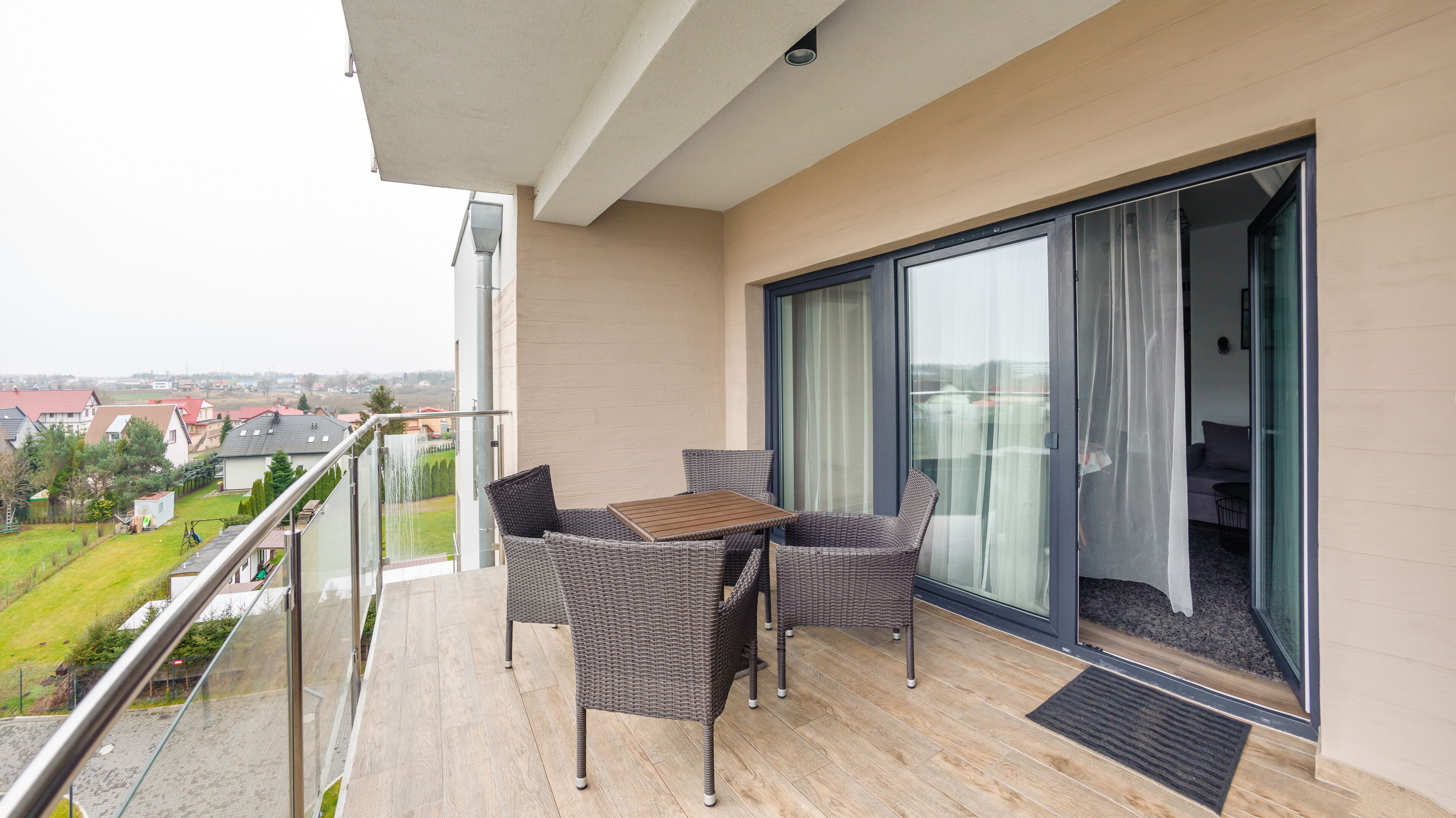 A balcony with wicker furniture, a sliding glass door, and a view of the neighborhood.