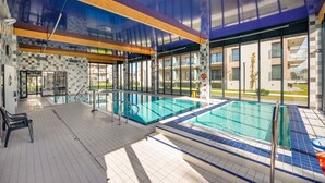 An indoor swimming pool with clear glass walls, a tiled floor, and a wooden ceiling. - Apartamenty Sun & Snow Piec Morz (Ustronie Morskie)