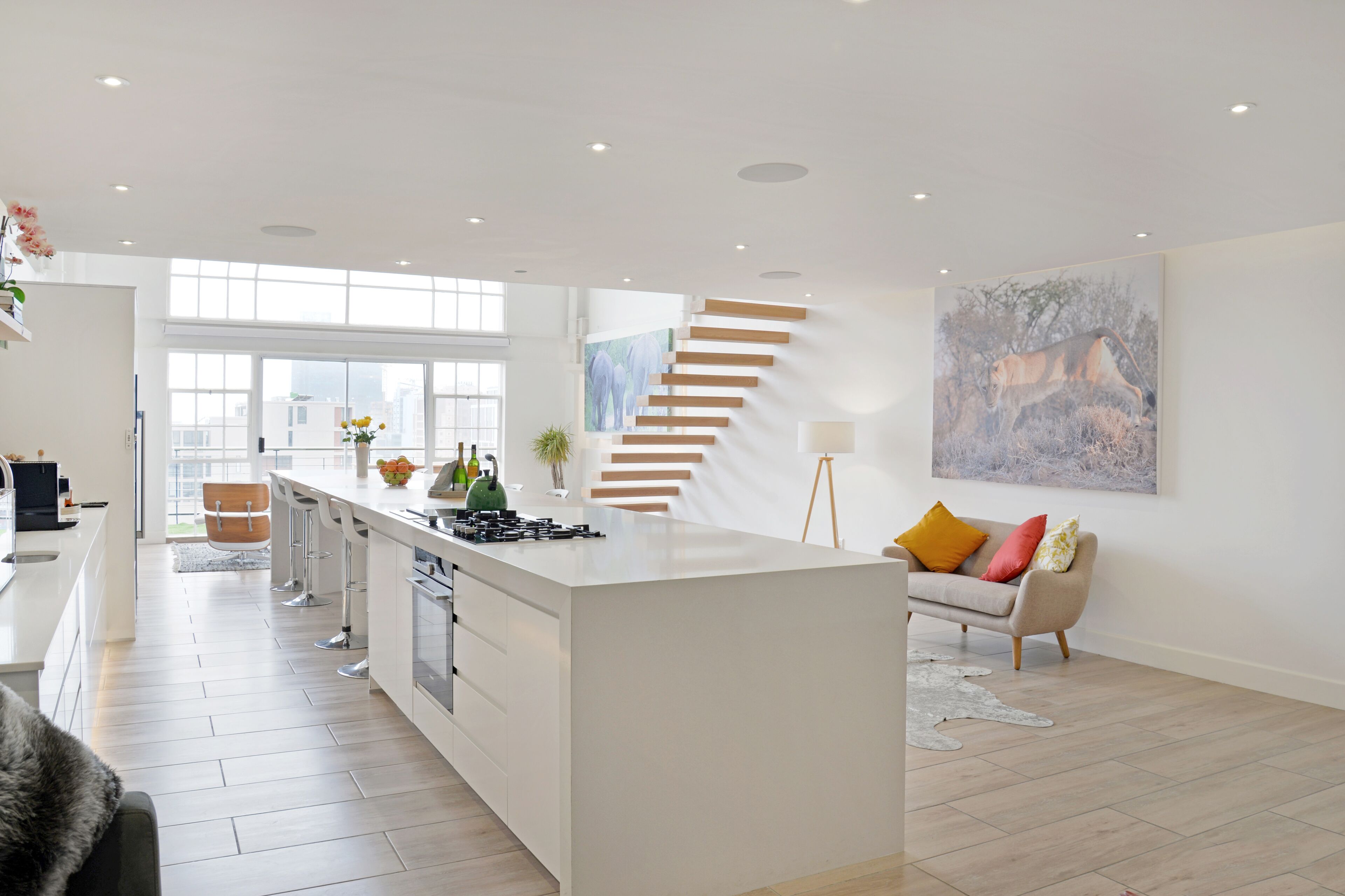 A modern kitchen with a central island, a staircase, and a dining area with a sofa.