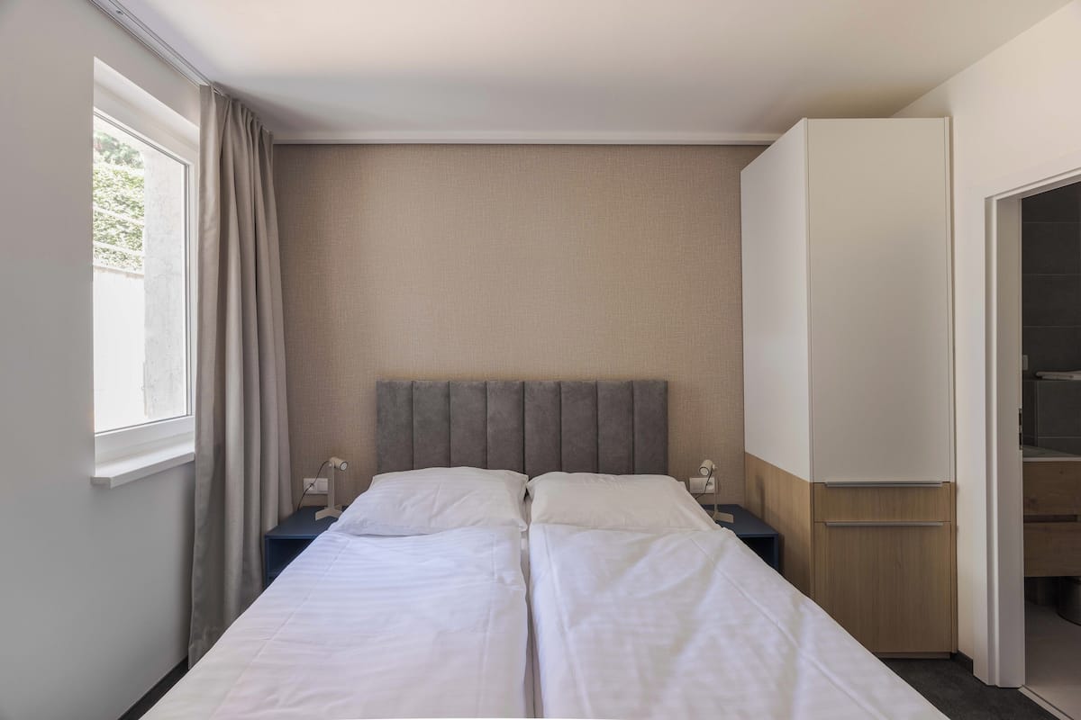 A hotel room with a bed, a nightstand, a wardrobe, and a window with curtains.