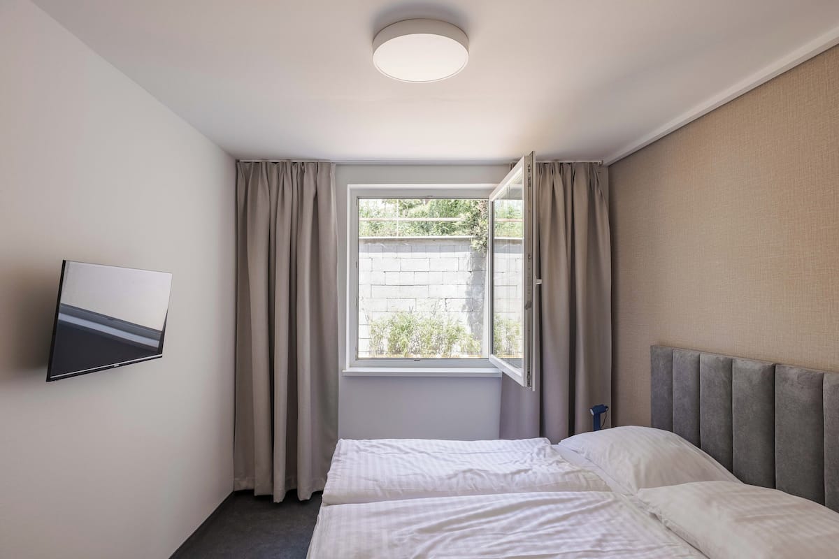 A hotel room with a bed, a flat-screen TV, a window with curtains, and a ceiling light.