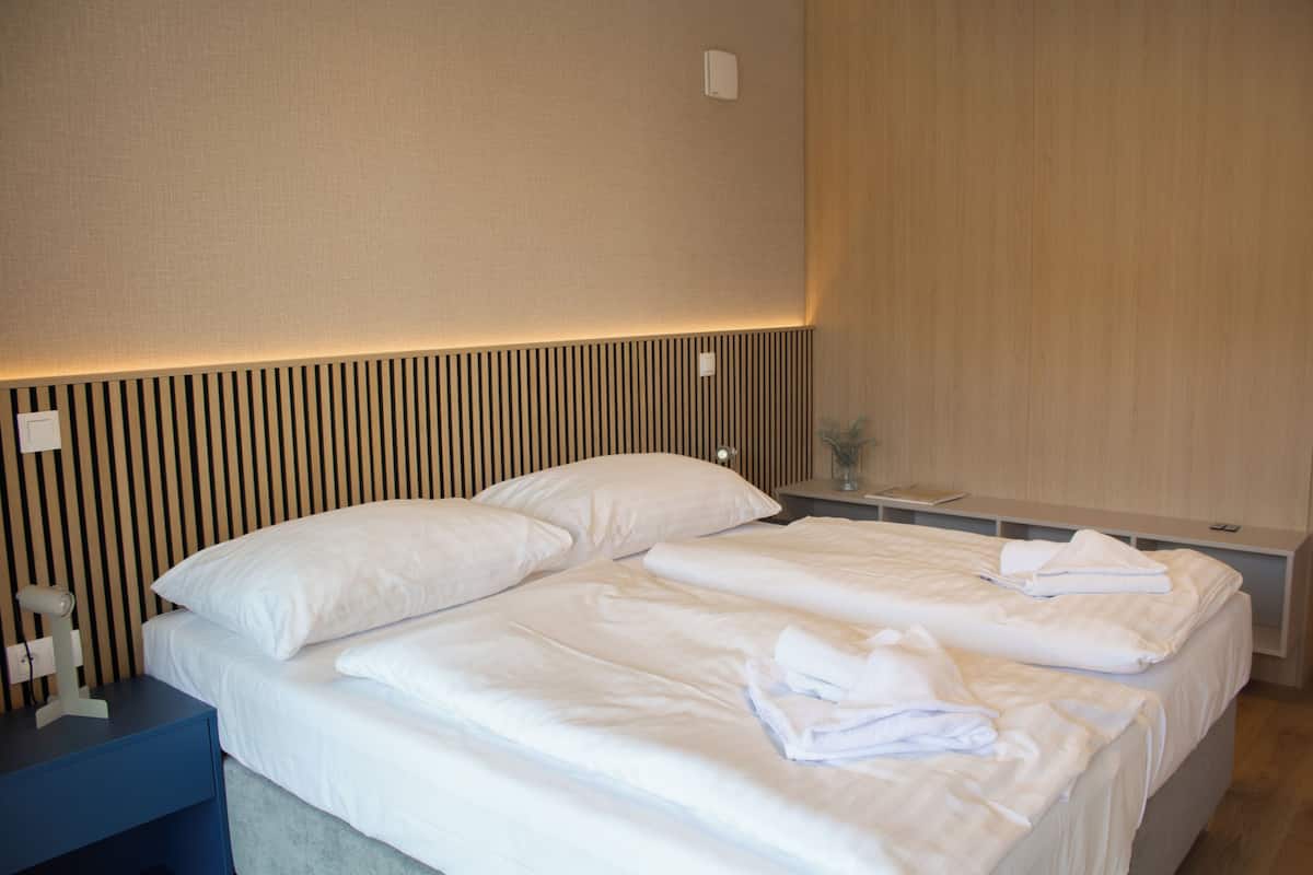 A hotel room with a bed, bedside tables, and a wall-mounted light fixture.