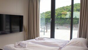 A hotel room with a bed, a TV mounted on the wall, and a balcony with a view of greenery. - Hotel Gardinn - Free Parking and Quiet Garden (Bratislava)