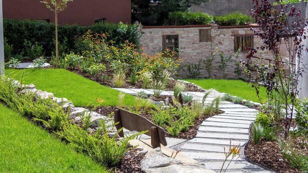 A landscaped garden with a stone pathway, a bench, and various plants. - Hotel Gardinn - Free Parking and Quiet Garden (Bratislava)