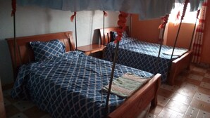 A room with two wooden beds, each with a patterned blue bedspread and a canopy. There is a small wooden table between the beds. - Kings Guest House (Kabati)