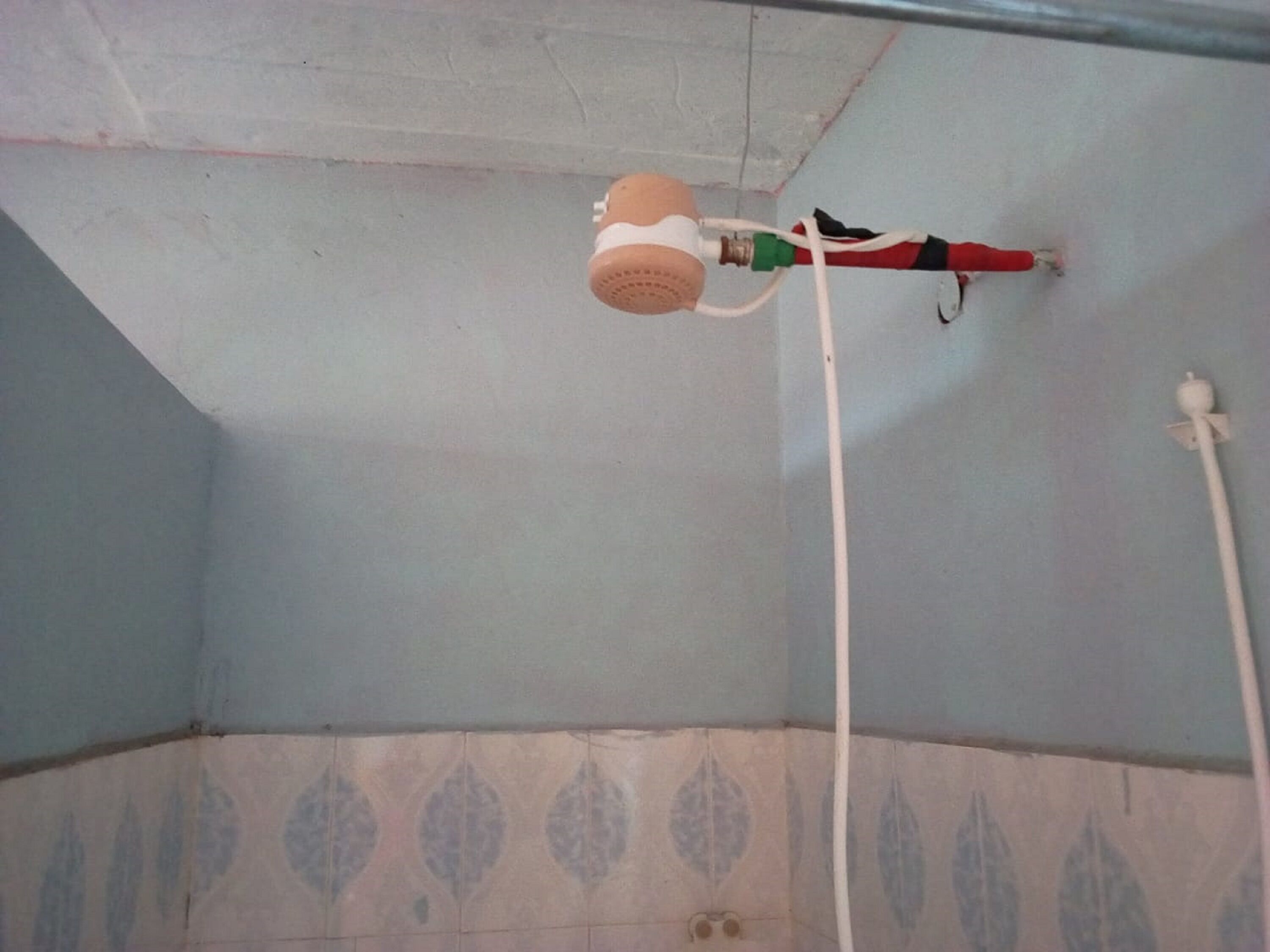 Une salle de bain avec un ventilateur de plafond, une tuyauterie apparente et un mur orné d’un motif décoratif.