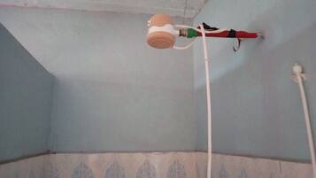 Une salle de bain avec un ventilateur de plafond, une tuyauterie apparente et un mur orné d’un motif décoratif.
