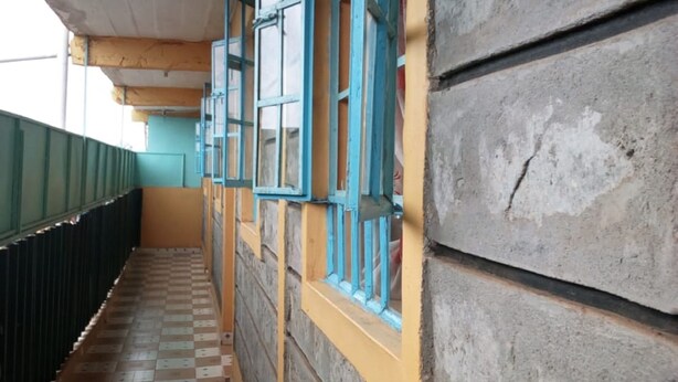 A corridor with checkered floor tiles, blue-framed windows, and a green wall. - Kings Guest House (Kabati)