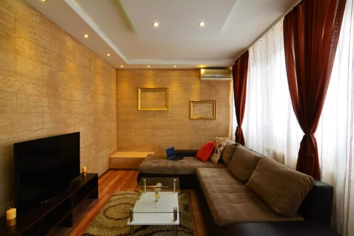 A modern living room with a flat-screen TV, a sofa, a coffee table, and a fireplace.