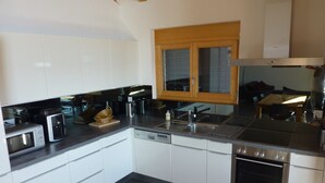 Una cocina moderna con armarios blancos, electrodomésticos de acero inoxidable y un ventanal sobre el fregadero.