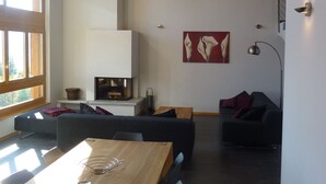 Una sala de estar moderna con una mesa de comedor de madera, sofás oscuros y una chimenea.
