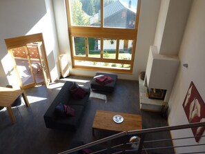 A spacious living area with a large window, a sofa, a coffee table, and a fireplace. - Appartement Loup-Blanc Est (Ayent)