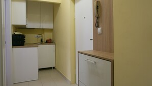 Een compacte keuken met witte kastjes, een klein aanrecht en een houten kastje met een telefoon.