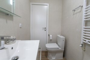A small, modern bathroom with a white sink, toilet, and glass shower enclosure.