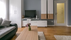 Een moderne woonkamer met een flatscreen televisie, witte kasten, een houten salontafel en een grijze bank.