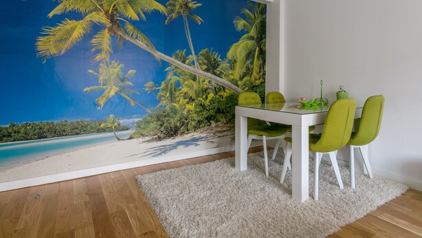 Een eetruimte met een tropische strandmuur, een witte tafel en groene stoelen.