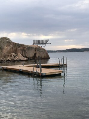 A wooden dock extending into calm water, with a metal ladder and a metal railing on top. - Farmlodge (Brastad)