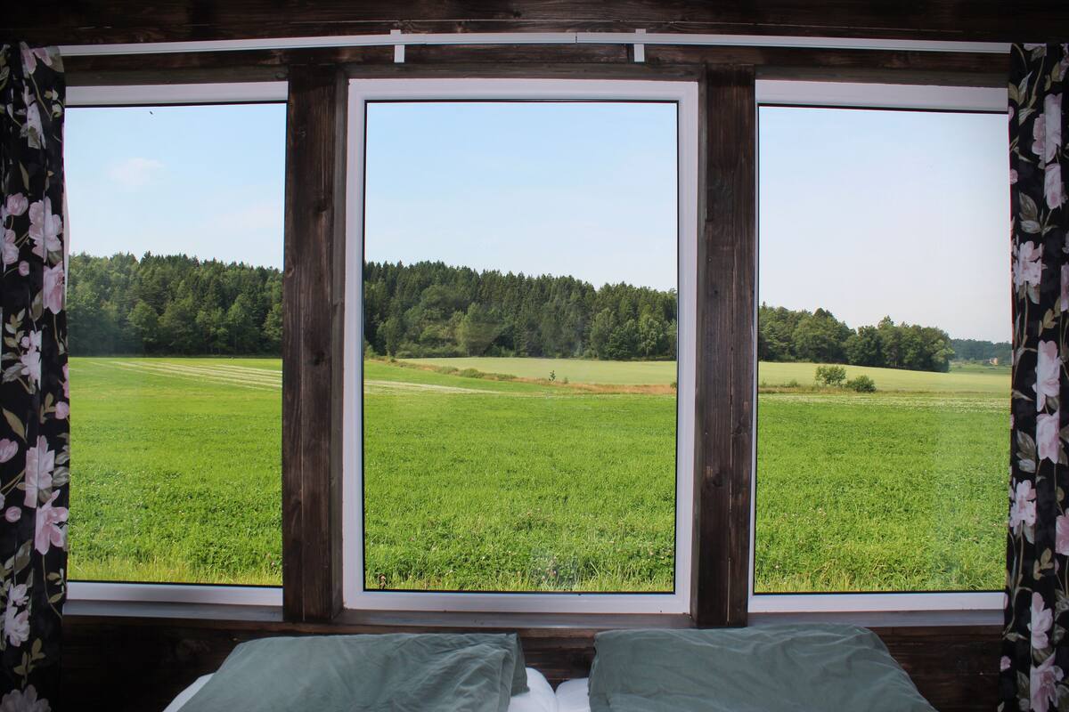 A room with a large window offering a view of a green field and forest.
