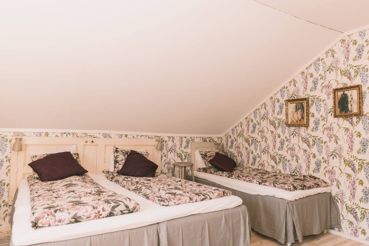 A bedroom with two single beds, floral wallpaper, and a small stool.