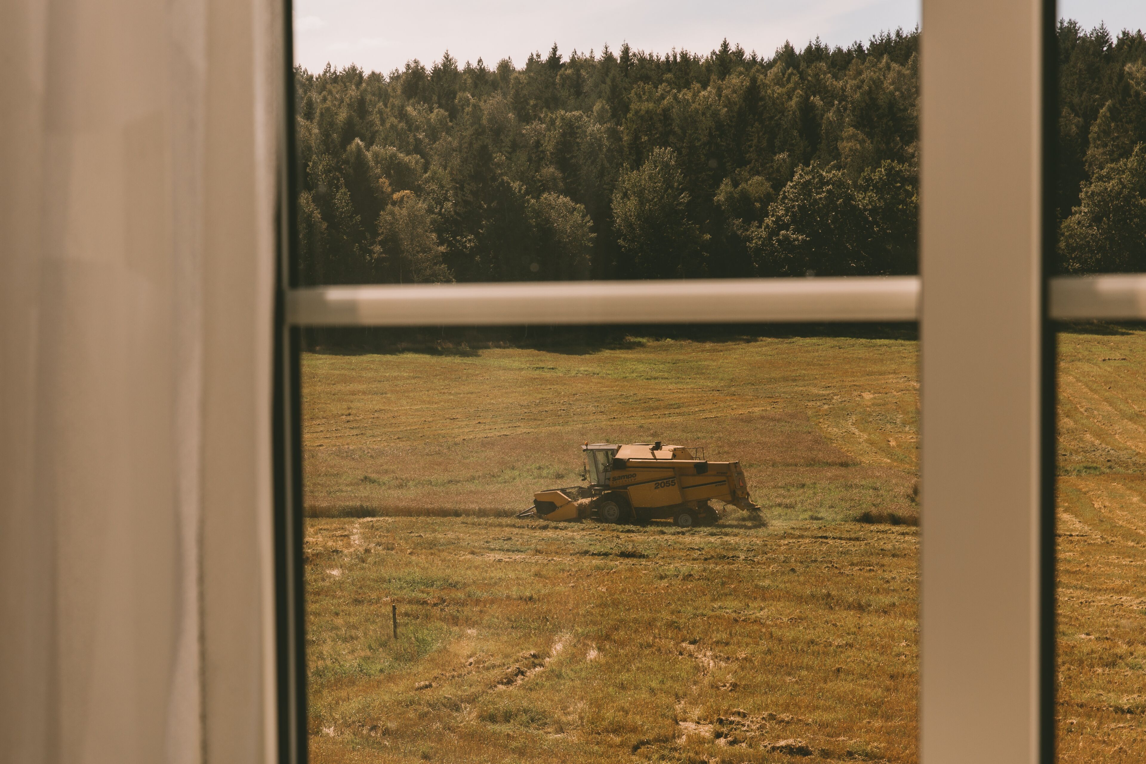 A view through a window of a field with a combine harvester.