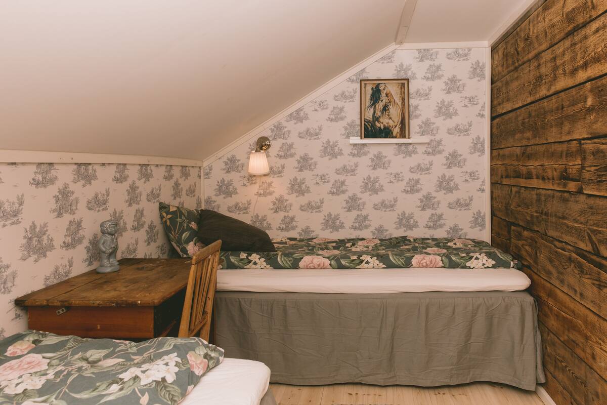 A small, cozy bedroom with a wooden headboard, a single bed with a floral bedspread, a nightstand with a lamp, and a small statue.