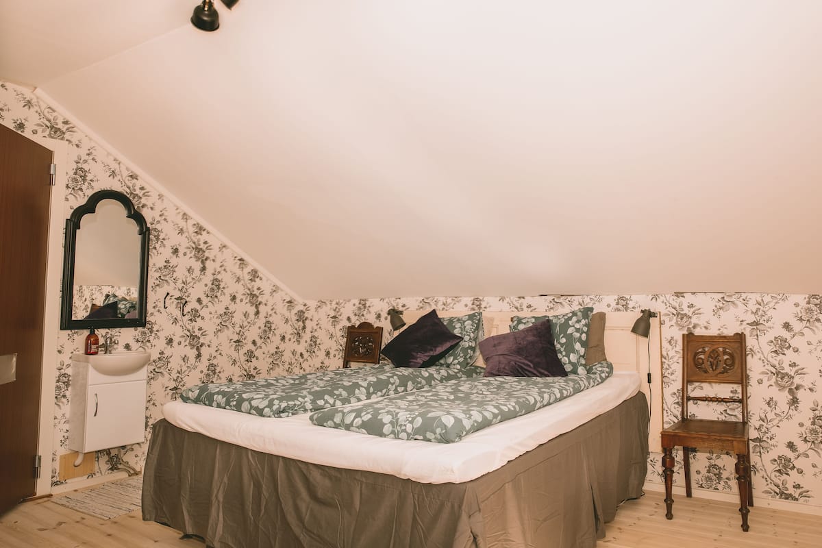 A bedroom with a bed, a wooden chair, a nightstand, a mirror, and a dresser.