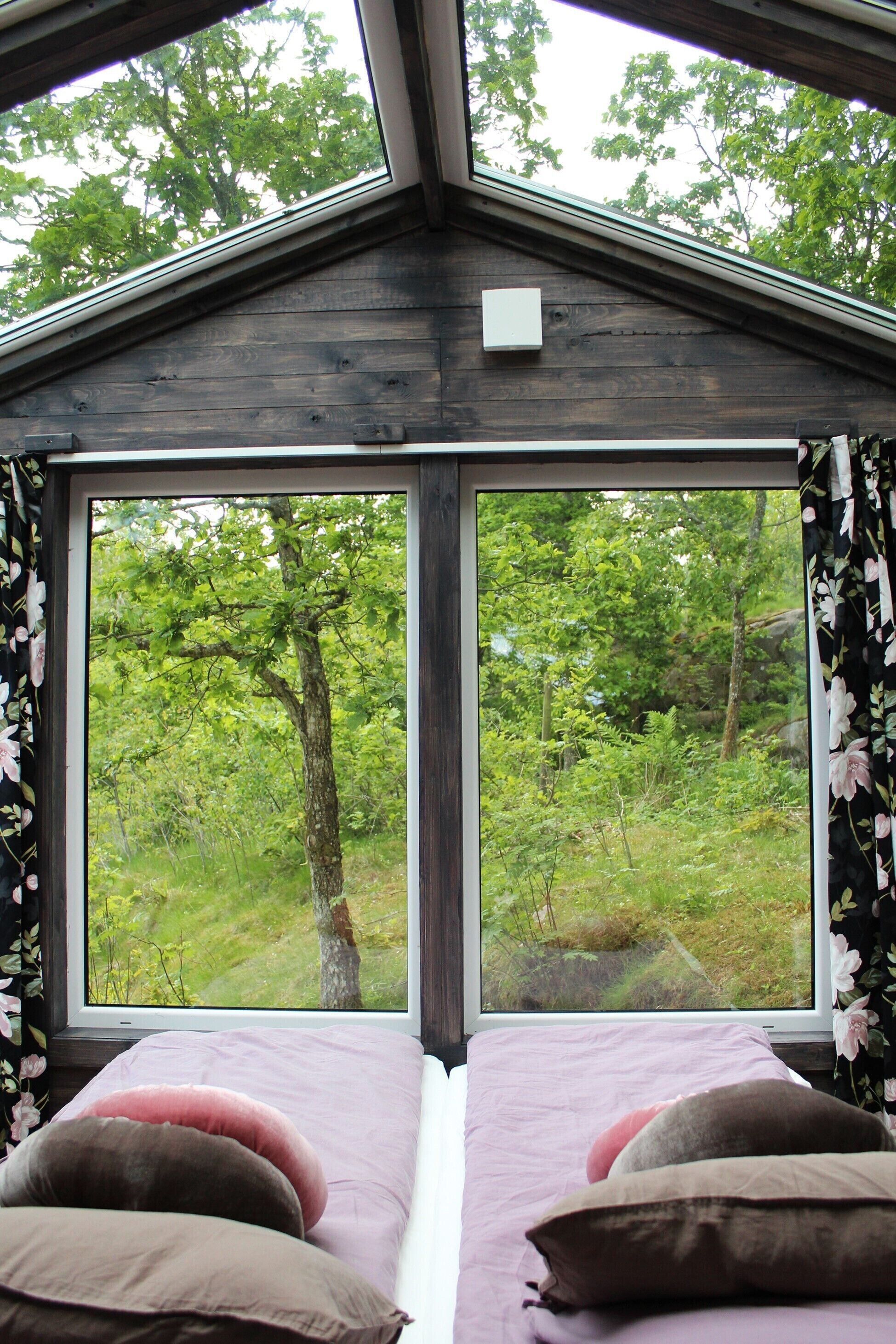 A bedroom with a large window overlooking a forest. There are two beds with pink and brown bedding.