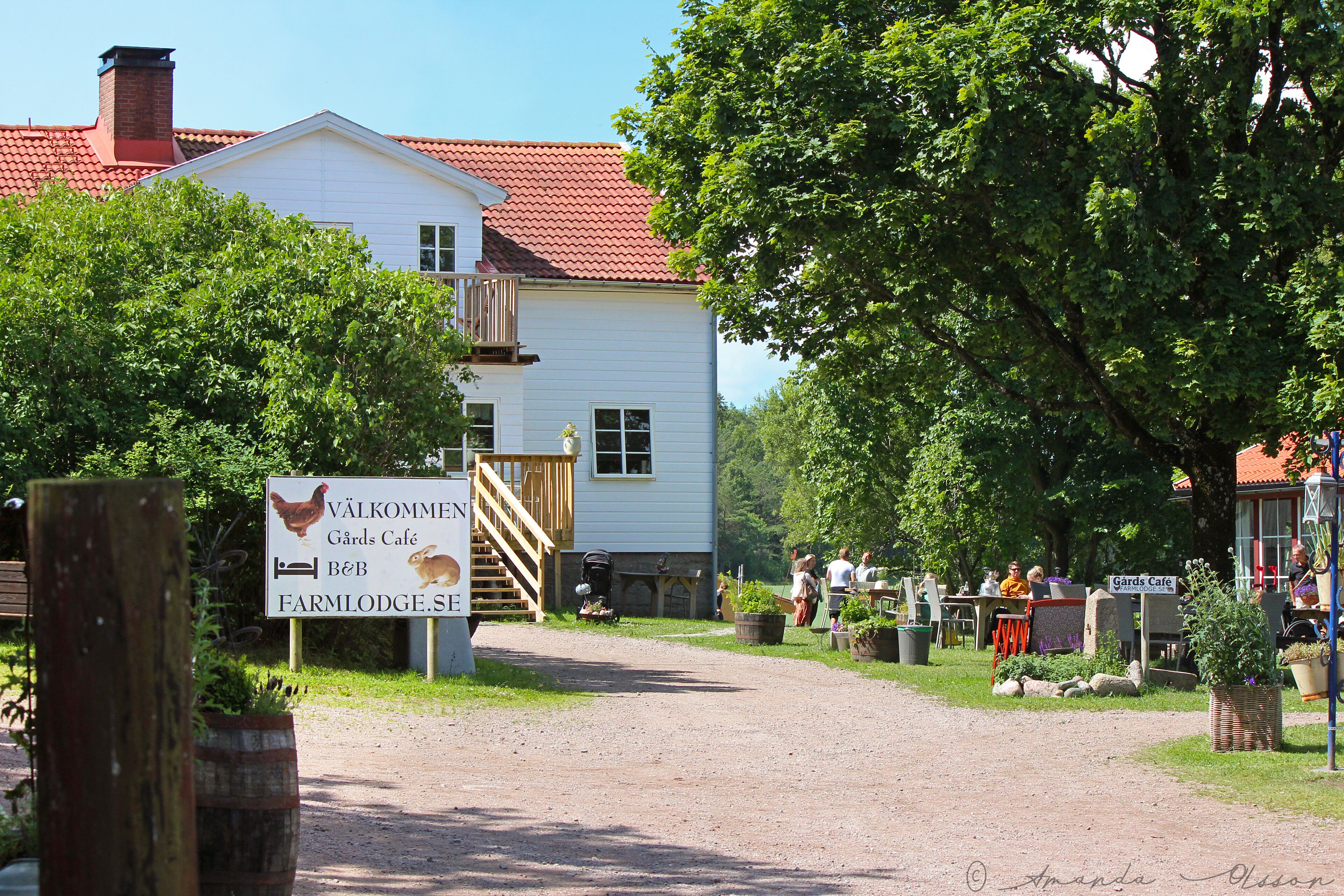 Un edificio blanco con techo rojo, un cartel de Café Väklommen Gård y un área de estar al aire libre.