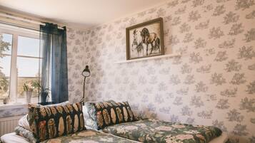 Una habitación con papel tapiz floral, una cama con ropa de cama estampada con flores, una ventana con cortinas y un cuadro en la pared.