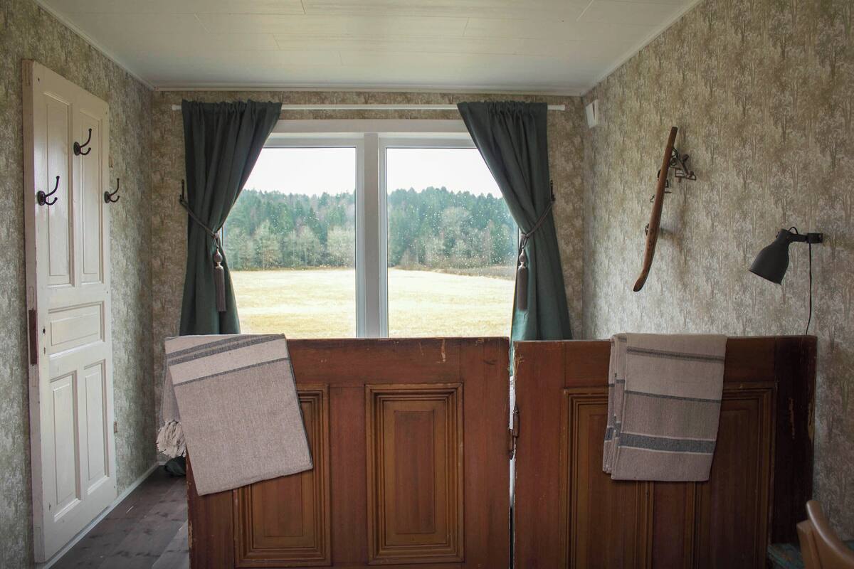A room with a large window, wooden doors, and a view of a forest.