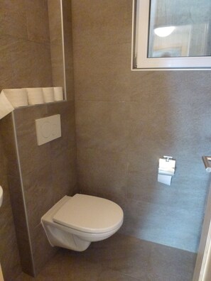 A small, modern bathroom with a toilet, a towel rack, and a window.