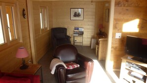 A cozy cabin interior with a leather sofa, a small table with a lamp, a television, and a framed picture on the wall. - Chalet Clématites (Ayent)