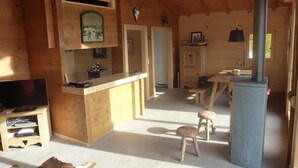 A wooden cabin interior with a kitchen area, a dining table, and a fireplace. - Chalet Clématites (Ayent)