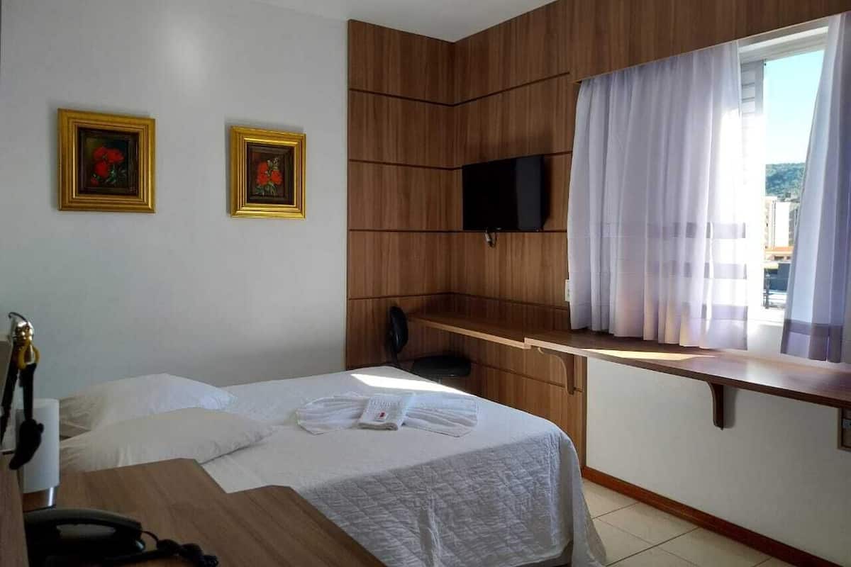 A hotel room with a bed, a desk, a TV, and a window with curtains.